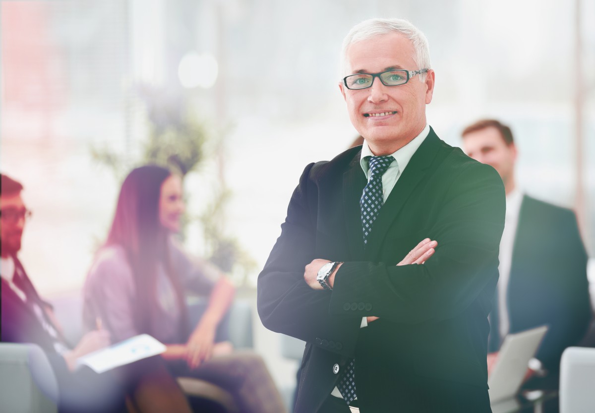 older businessman stands in front of group of younger employees244803921