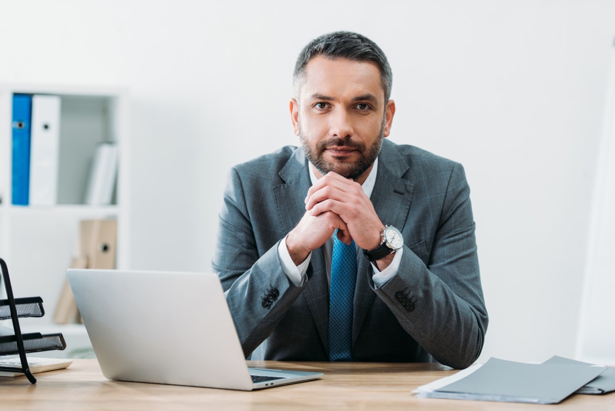 Financial Advisor faces camera while seated in front of laptop at desk 252883517